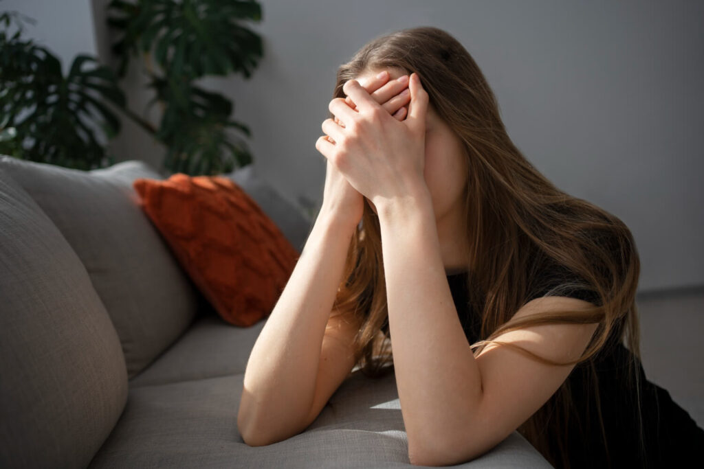 Young woman sitting anxiously with her hands covering her face