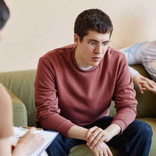 A young man in a therapy session with an unrecognizable partner sitting on the couch