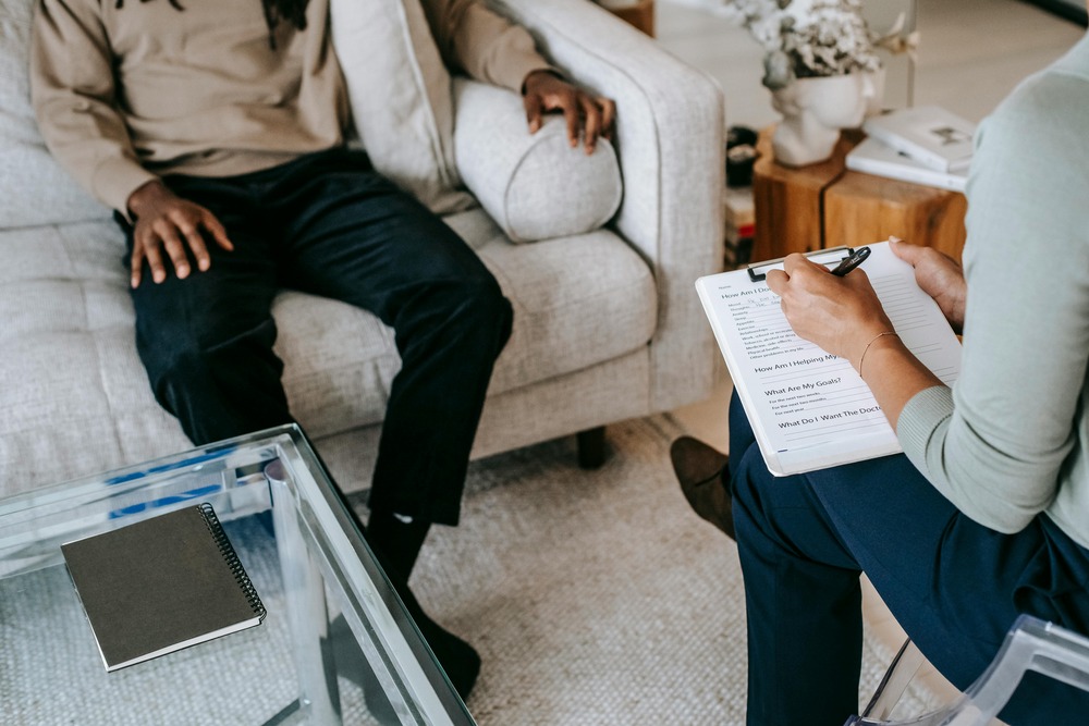 Top-angle shot over the shoulder of a woman sitting and taking notes on a clipboard while a man sits across from her.