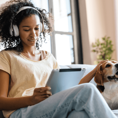 A woman sits at home with her dog while using her tablet for a virtual mental health therapy session
