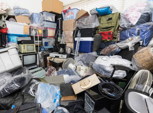 A hoarded room full of old appliances, books, linens bins of stuff, and miscellaneous items