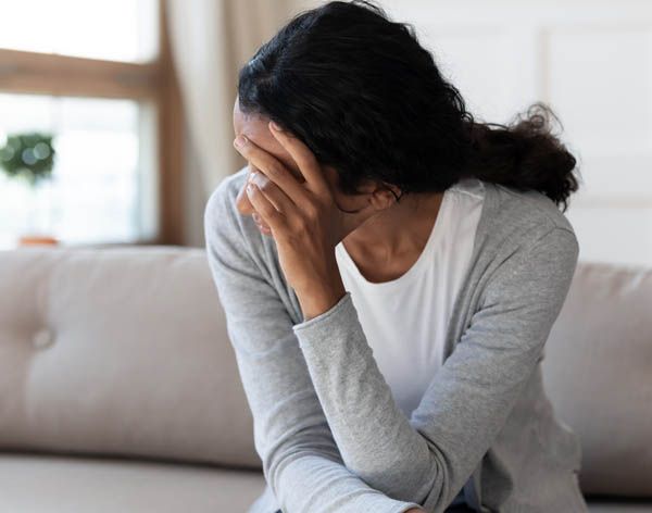 Young woman sitting on a couch with her head turned away from the camera one hand partially covering her face