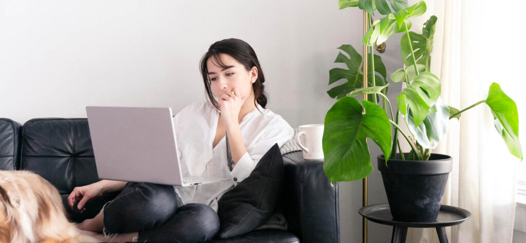 A young woman at home sits on the couch with a laptop for online therapy