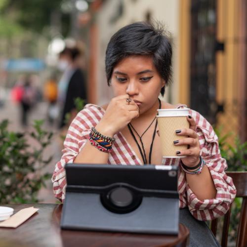 A woman outdoors drinking coffee and using her ipad for a virtual mental health call