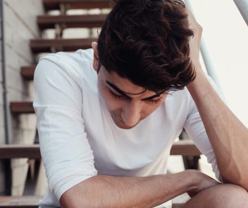 A young man sitting outdoors on apartment steps with his head down