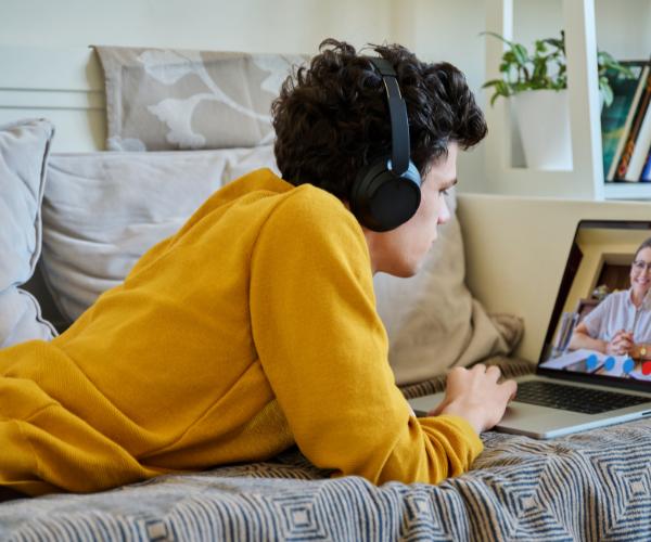 Young man at home lying on his stomach on the couch while using a laptop for online therapy