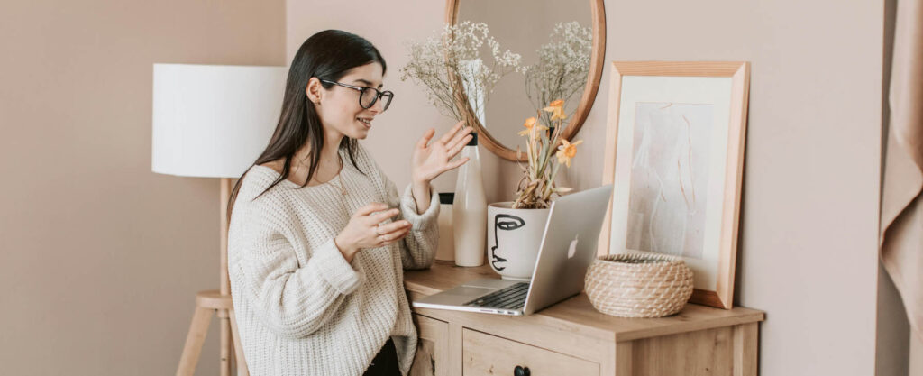 Young woman standing in a room with her laptop on a dresser for a virtual mental health session