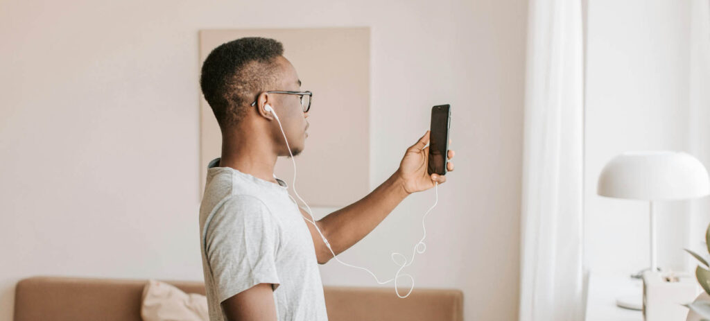 A young man is standing in his living room and using his phone for a mental health video call session