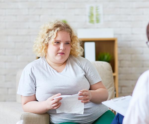 A sad young woman holds a facial tissue and looks on as a therapist takes notes