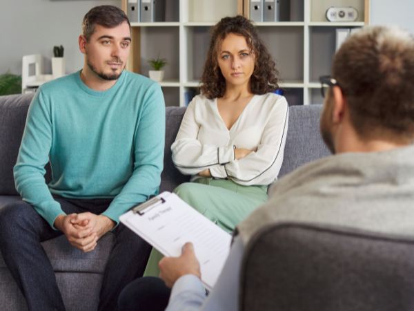 A young couple sitting on a couch and listening during a session with a mental health therapist