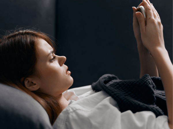A young woman is lying down at night, focused on her smart phone