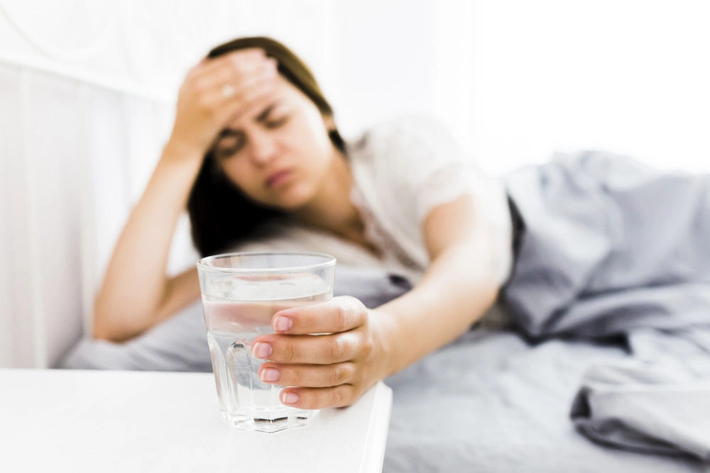 Young adult woman waking up with Sunday scaries and reaching for water