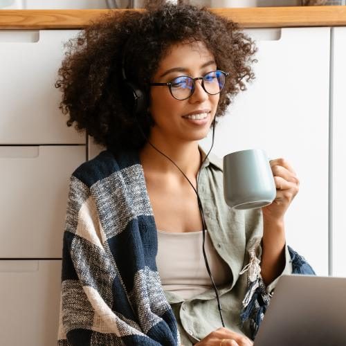 Young woman sitting on the floor, holding a coffee cup and using her laptop for an online therapy session