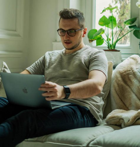 A young man sitting on a couch at home using his laptop for an online therapy session