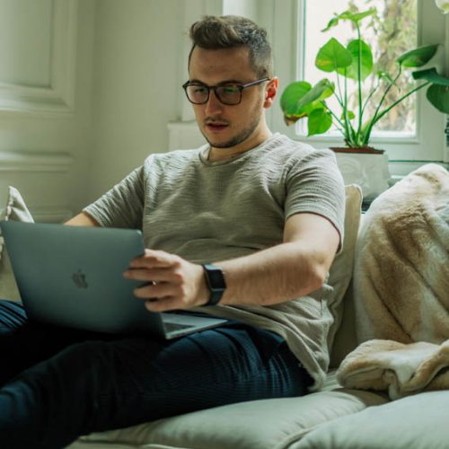 A young man sitting on a couch at home using his laptop for an online therapy session